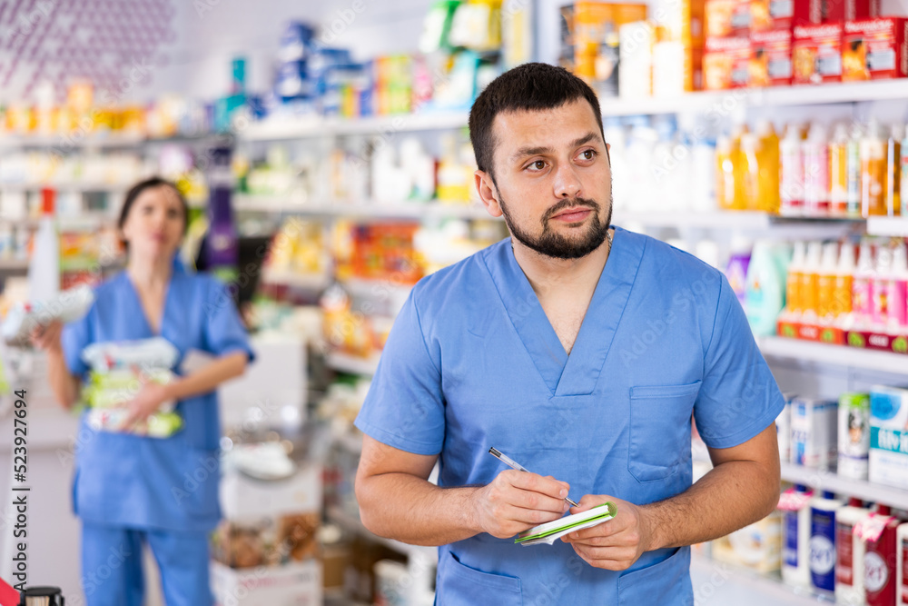 Diligent friendly male pharmacist noting assortment of drugs in pharmacy