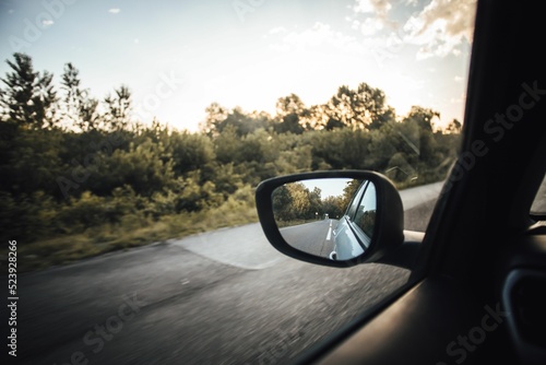 Closeup of a wing mirror reflecting the car's rear side while driving.