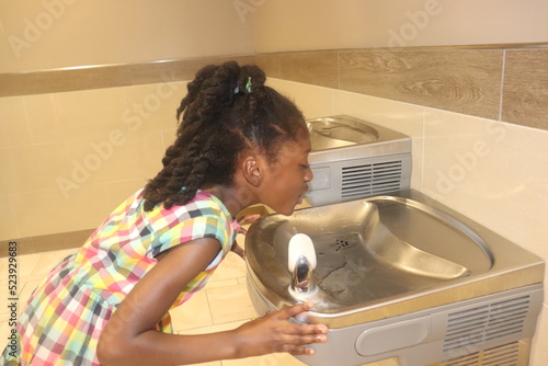 African American Kid drinking from water fountain indoors 