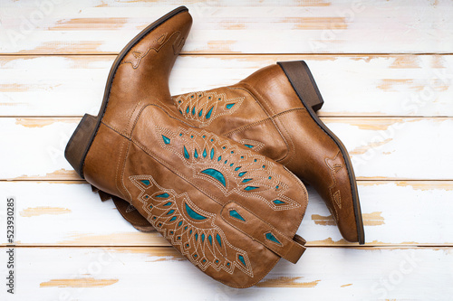 Women's fashion boots with a pattern. Ladies vintage leather cowboy shoes. On white floor boards.