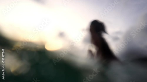 Low angle view of Asian woman surfer paddling surfboard and riding the wave in the sea at tropical beach at sunset. Girl friends enjoy outdoor lifestyle and water sport surfing on summer vacation