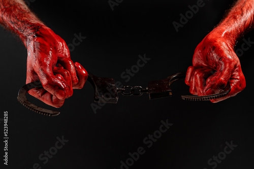 A man with bloody hands holds iron handcuffs. © Михаил Решетников