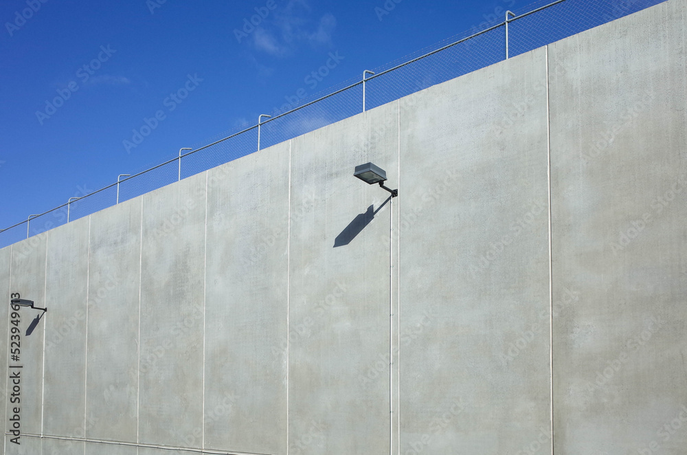Obraz premium A large high urban blank wall in natural sunlight against blue sky with copy space room to add your own text or banner. Industrial background texture of concrete warehouse with street lights.