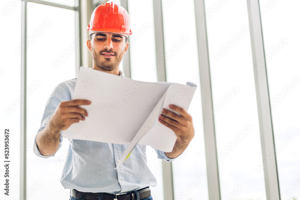 Professional of architect industrial engineer cargo man in helmet working new construction project architectural plan with blueprint and construction tool on table at the building construction site Professional of architect industrial engineer cargo man in helmet working new construction project architectural plan with blueprint and construction tool on table at the building construction site