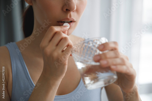 A young woman takes medications or vitamins. She's holding a glass of water.