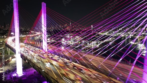 An aerial time lapse of vehicles travelling on the Kosciuszko Bridge lit up with colorful light emitting diodes. The NYC skyline is in the background as the camera dolly in, pan right then dolly out. photo