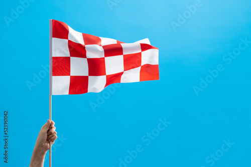 Human hand waving checkered flag on blue background