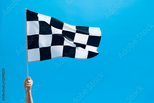 Human hand waving checkered flag on blue background