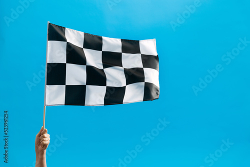 Human hand waving checkered flag on blue background © xy
