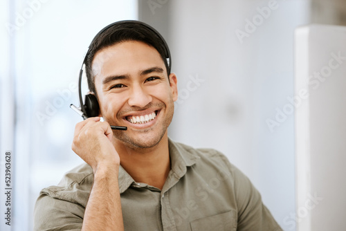 Smiling, friendly call center agent with headset for online consulting in an IT tech agency. Face of male ecommerce support professional offering virtual assistance to web user or contact us hotline