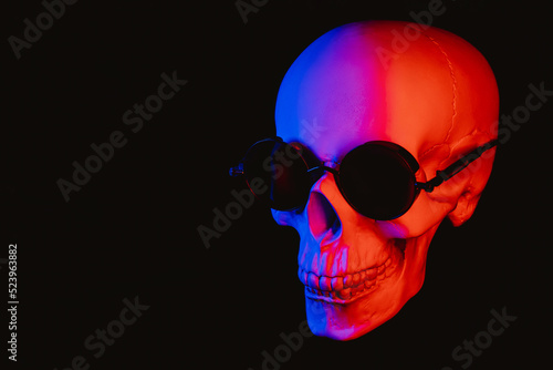 human skull wearing sunglasses with colored neon light on a dark background