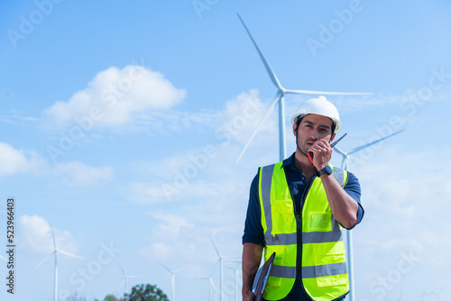 Engineer wearing uniform ,helmet inspection and survey work in wind turbine farms rotation to generate electricity energy. Green ecological power energy generation wind sustainable energy concept.