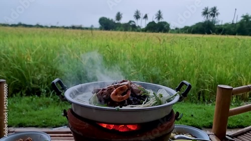 Grilling Thai pork barbecue on a pan in the hut along with a view over the rice fields. Cooking grilled bbq for dinner. Korean bbbq photo