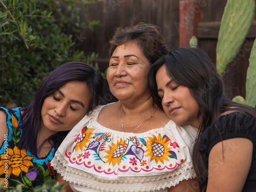 Horizontal close-up image of Indigenous women closing their eyes and standing closing together 