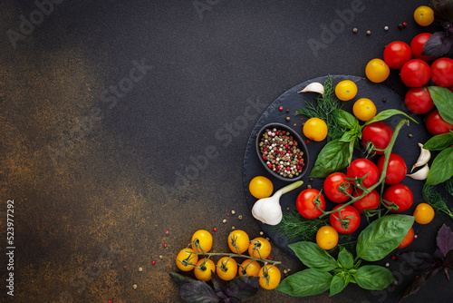 Food background, fresh ripe red and yellow tomatoes, spices and basil leaves, garlic and green onions on a dark board, healthy food concept, copy space, top view