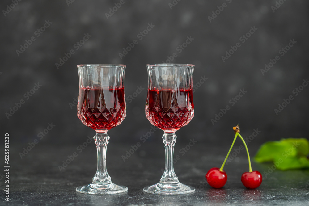 Homemade cherry brandy in two crystal glasses on a black background Homemade cherry brandy in two crystal glasses on a black background