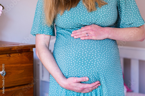 Young pregnant woman in her twenties standing near cot in nursery photo