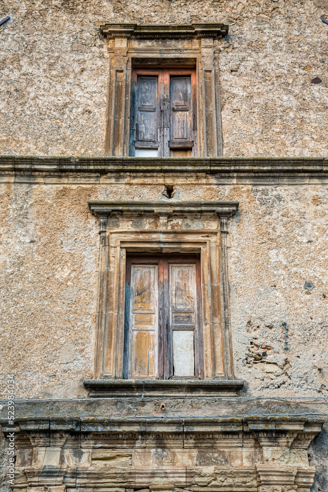 Closeup of a wooden frame window on ancient house in a village. A small window and grey stone or brick wall of an old antique building in Italy.
