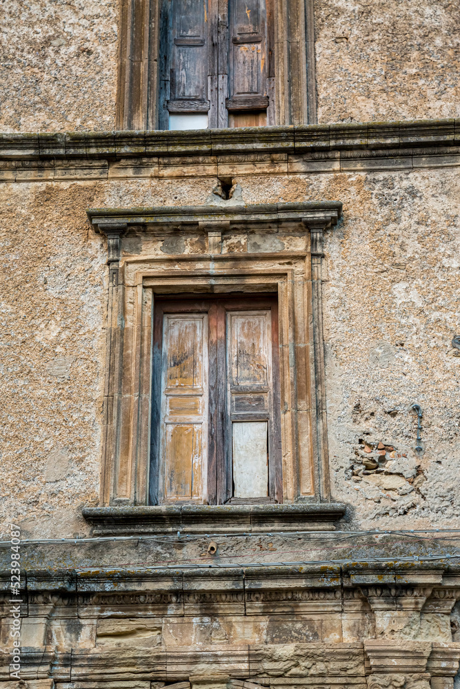 Closeup of a wooden frame window on ancient house in a village. A small window and grey stone or brick wall of an old antique building in Italy.