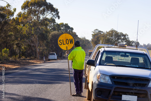 worker holding slow lollipop sign on edge of road near vehicle photo