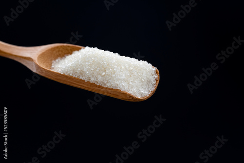 Wooden scoop with sugar crystals on black background