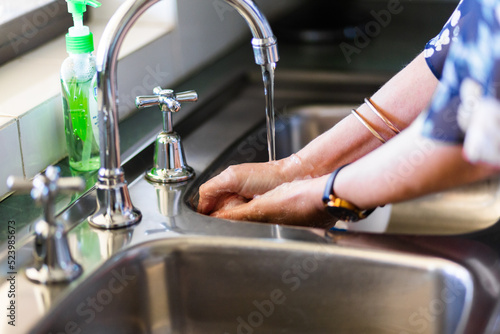 senior woman washing hands with soap in the kitchen sink photo