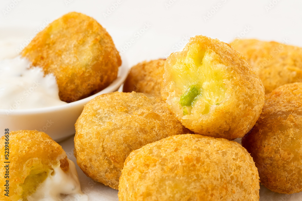 Detail of fried breaded chilli cheese nuggets next to a bowl of white sauce. One eaten.