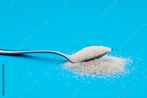 Steel spoon with sugar crystals on blue background