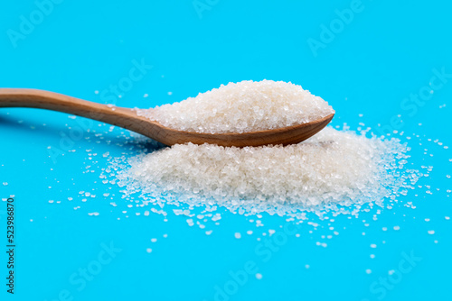 Wooden spoon with sugar crystals on blue background
