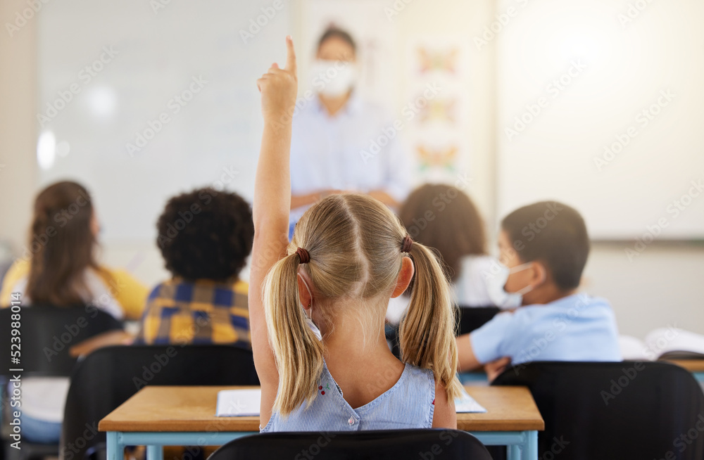 Learning, smart and little girl in class holding up a hand to answer a question at school. Back view of a young student sitting at a classroom desk looking to solve the questions a teacher is asking Learning, smart and little girl in class holding up a hand to answer a question at school. Back view of a young student sitting at a classroom desk looking to solve the questions a teacher is asking