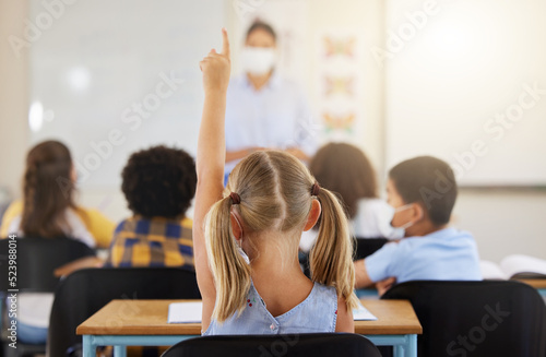 Learning, smart and little girl in class holding up a hand to answer a question at school. Back view of a young student sitting at a classroom desk looking to solve the questions a teacher is asking © Nina Lawrenson/peopleimages.com