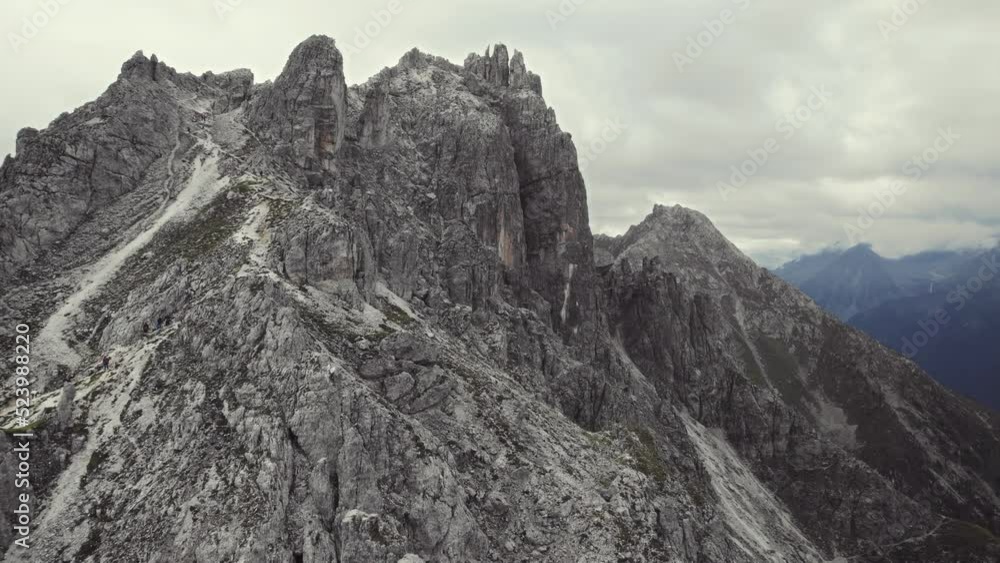 Beautiful aerial of alpine mountains 11er (Stubai, Austria). Passing stone formations while flying torwads the peak with a cross on top. Picturesque mountain scenery in the background on a cloudy day Beautiful aerial of alpine mountains 11er (Stubai, Austria). Passing stone formations while flying torwads the peak with a cross on top. Picturesque mountain scenery in the background on a cloudy day
