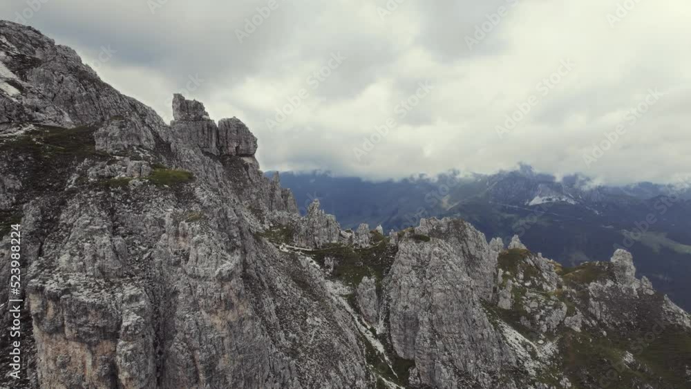 Beautiful aerial of alpine mountains 11er (Stubai, Austria). Passing grassy stone formations revealing a small hiking trail. Alpine mountain scenery and a valley in the background on a cloudy day. 4K