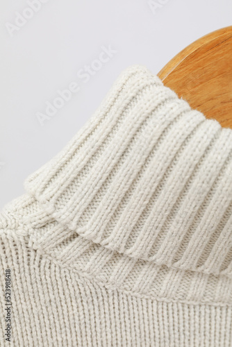 Wooden hanger with sweater on light background, close up