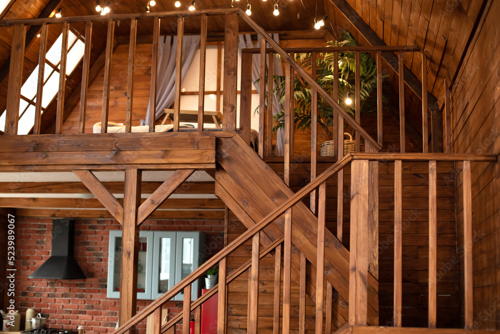 Wooden Stairway goes up. Country wooden house is spacious on two levels. Room with wooden stairway leading to second floor of modern flat. Modern staircase with wooden steps in flat. Wooden Stairway goes up. Country wooden house is spacious on two levels. Room with wooden stairway leading to second floor of modern flat. Modern staircase with wooden steps in flat.