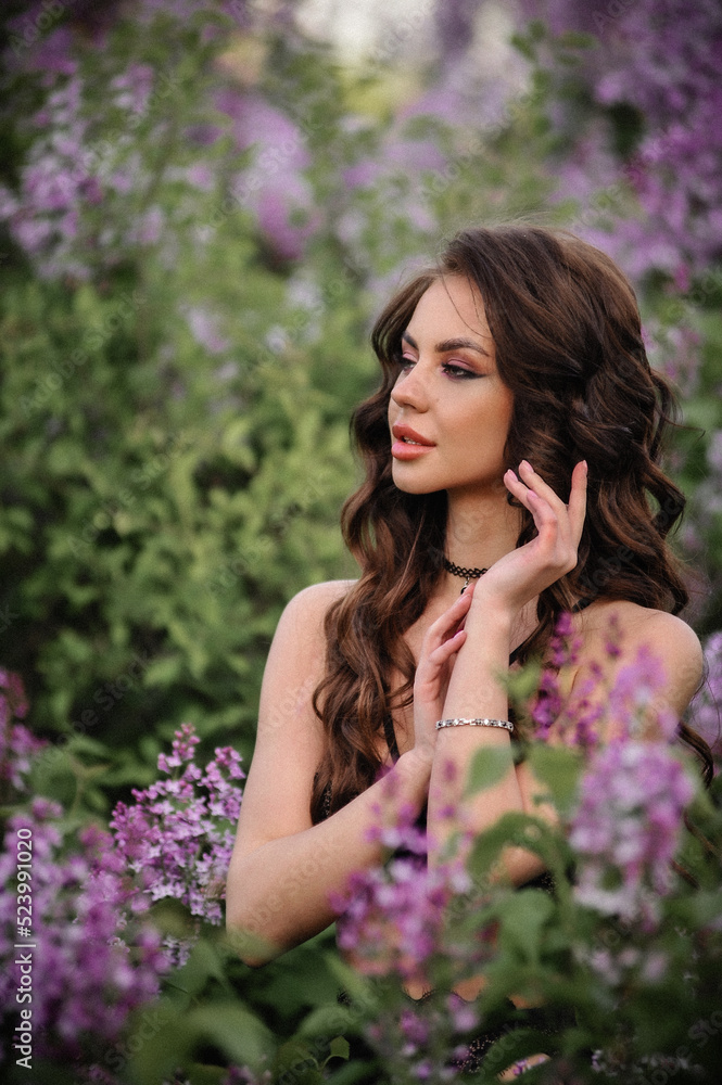 a beautiful girl with makeup and hair styling in underwear stands in a garden with lilacs on a summer evening a beautiful girl with makeup and hair styling in underwear stands in a garden with lilacs on a summer evening