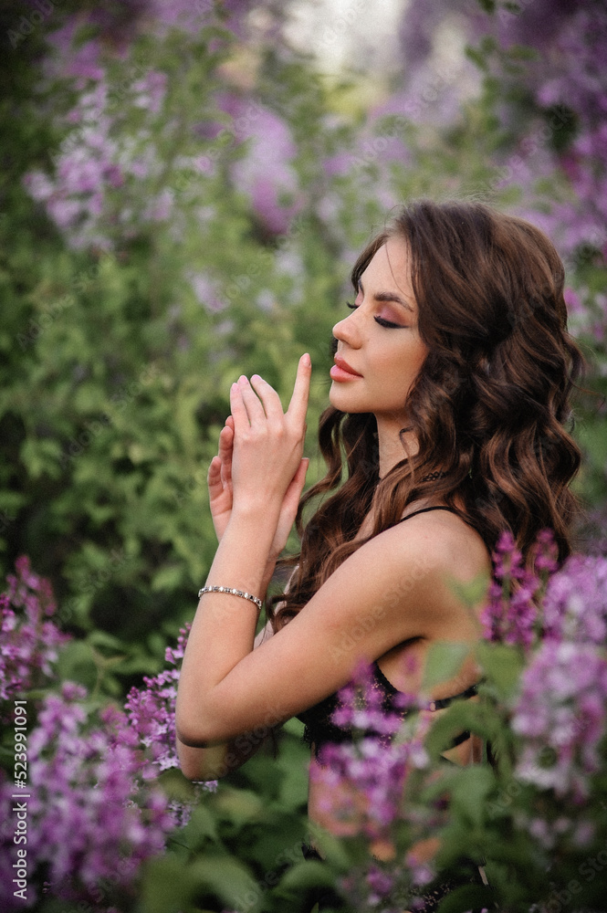a beautiful girl with makeup and hair styling in underwear stands in a garden with lilacs on a summer evening a beautiful girl with makeup and hair styling in underwear stands in a garden with lilacs on a summer evening