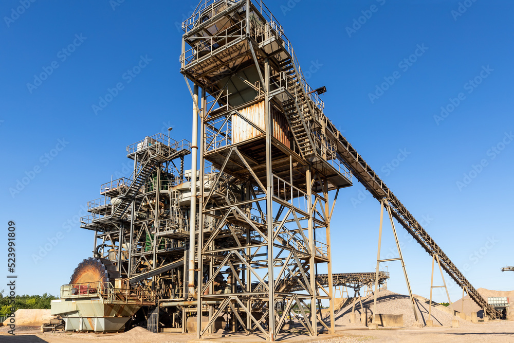 Panoramic view heavy metal construction open pit gravel plant sand quarry big rusty rotor machine material excavating and crushing on blue sky. Industrial machinery factory equipment steel background Panoramic view heavy metal construction open pit gravel plant sand quarry big rusty rotor machine material excavating and crushing on blue sky. Industrial machinery factory equipment steel background