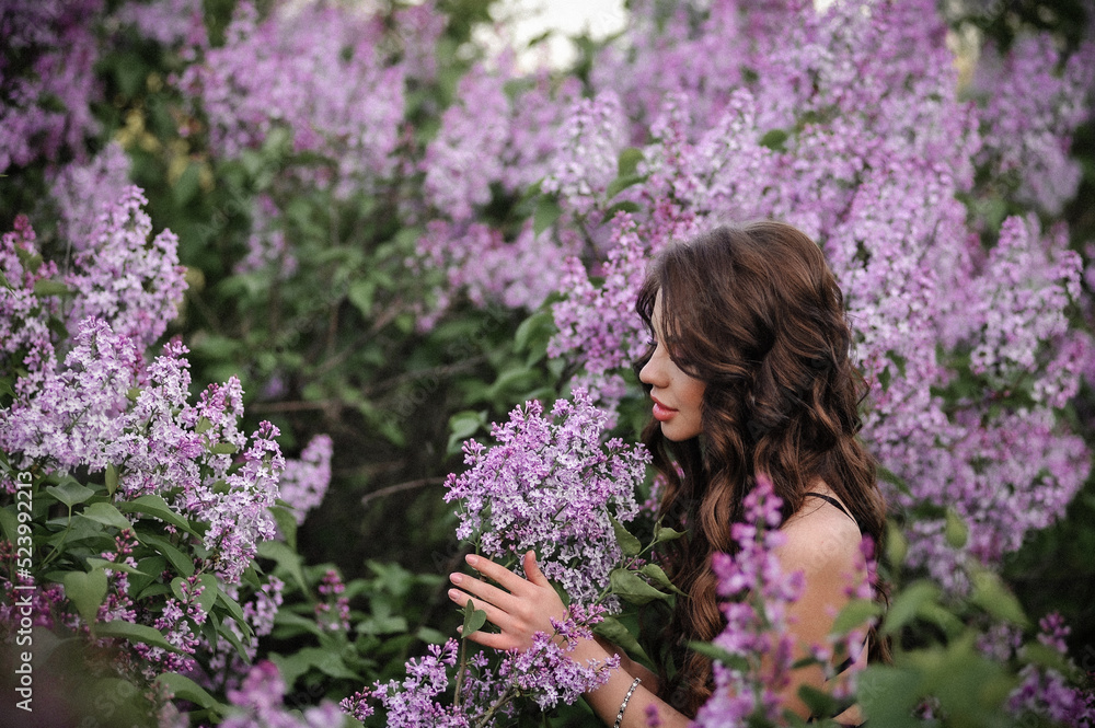 a beautiful girl with makeup and hair styling in underwear stands in a garden with lilacs on a summer evening a beautiful girl with makeup and hair styling in underwear stands in a garden with lilacs on a summer evening