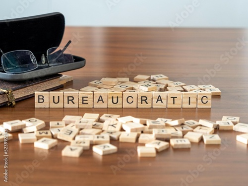 bureaucratic word or concept represented by wooden letter tiles on a wooden table with glasses and a book photo