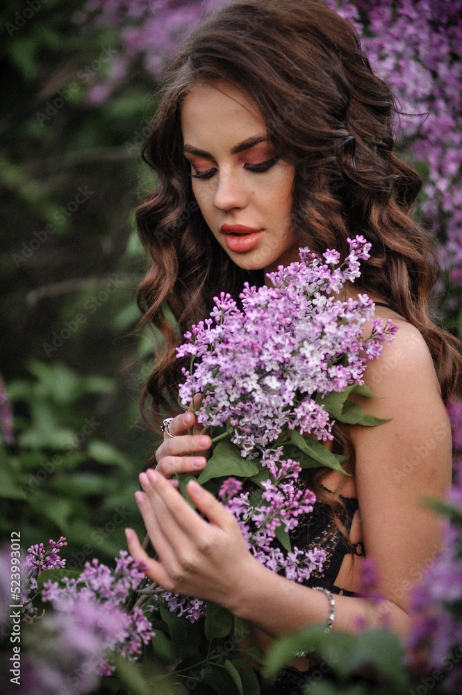 a beautiful girl with makeup and hair styling in underwear stands in a garden with lilacs on a summer evening a beautiful girl with makeup and hair styling in underwear stands in a garden with lilacs on a summer evening