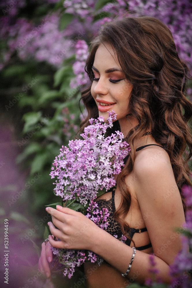 a beautiful girl with makeup and hair styling in underwear stands in a garden with lilacs on a summer evening a beautiful girl with makeup and hair styling in underwear stands in a garden with lilacs on a summer evening