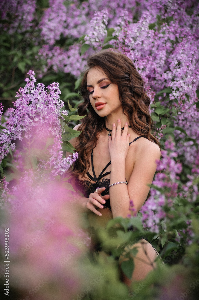 a beautiful girl with makeup and hair styling in underwear stands in a garden with lilacs on a summer evening a beautiful girl with makeup and hair styling in underwear stands in a garden with lilacs on a summer evening