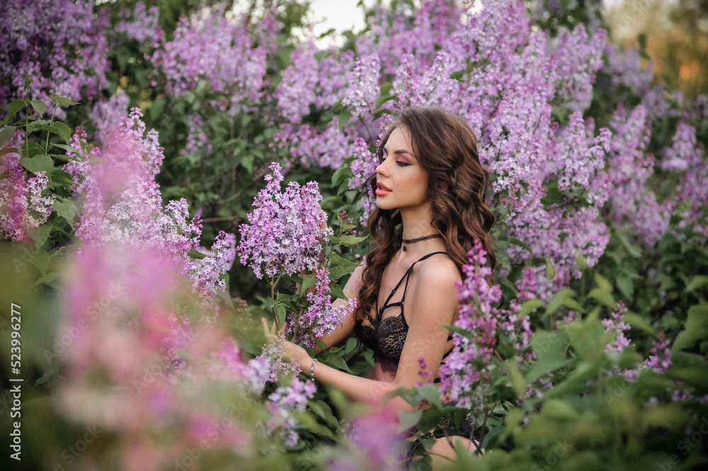 a beautiful girl with makeup and hair styling in underwear stands in a garden with lilacs on a summer evening a beautiful girl with makeup and hair styling in underwear stands in a garden with lilacs on a summer evening