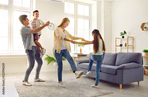 Happy, joyful family having fun at home. Cheerful, carefree mother, father and children spending time in their spacious modern living room, playing games and dancing