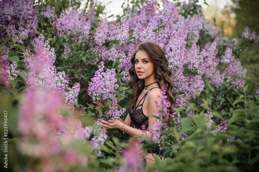 a beautiful girl with makeup and hair styling in underwear stands in a garden with lilacs on a summer evening a beautiful girl with makeup and hair styling in underwear stands in a garden with lilacs on a summer evening