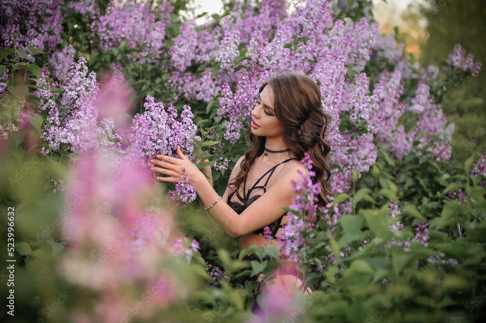 a beautiful girl with makeup and hair styling in underwear stands in a garden with lilacs on a summer evening a beautiful girl with makeup and hair styling in underwear stands in a garden with lilacs on a summer evening