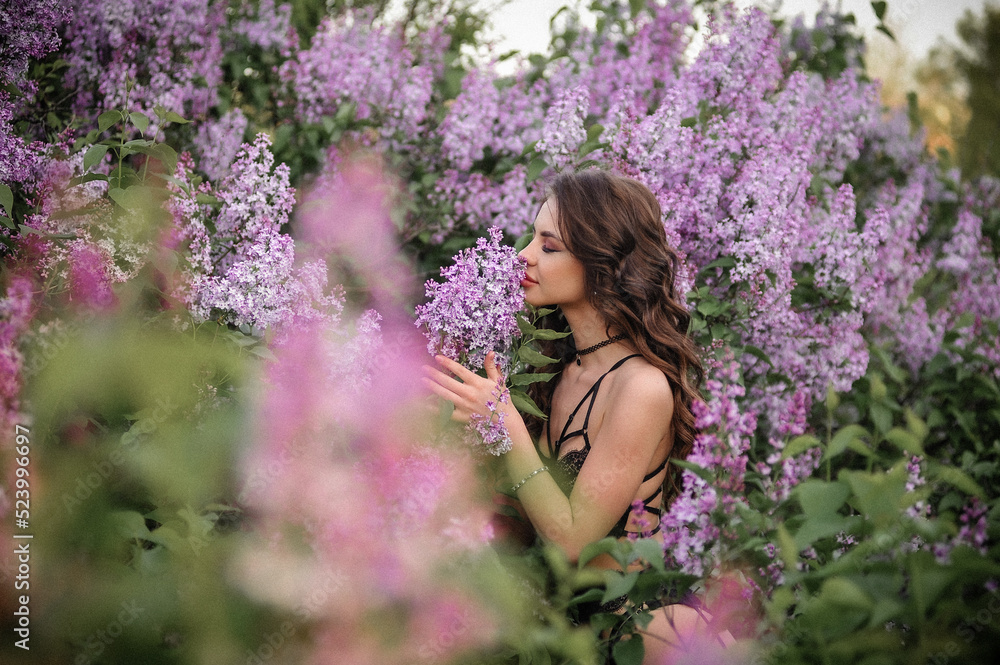 a beautiful girl with makeup and hair styling in underwear stands in a garden with lilacs on a summer evening a beautiful girl with makeup and hair styling in underwear stands in a garden with lilacs on a summer evening