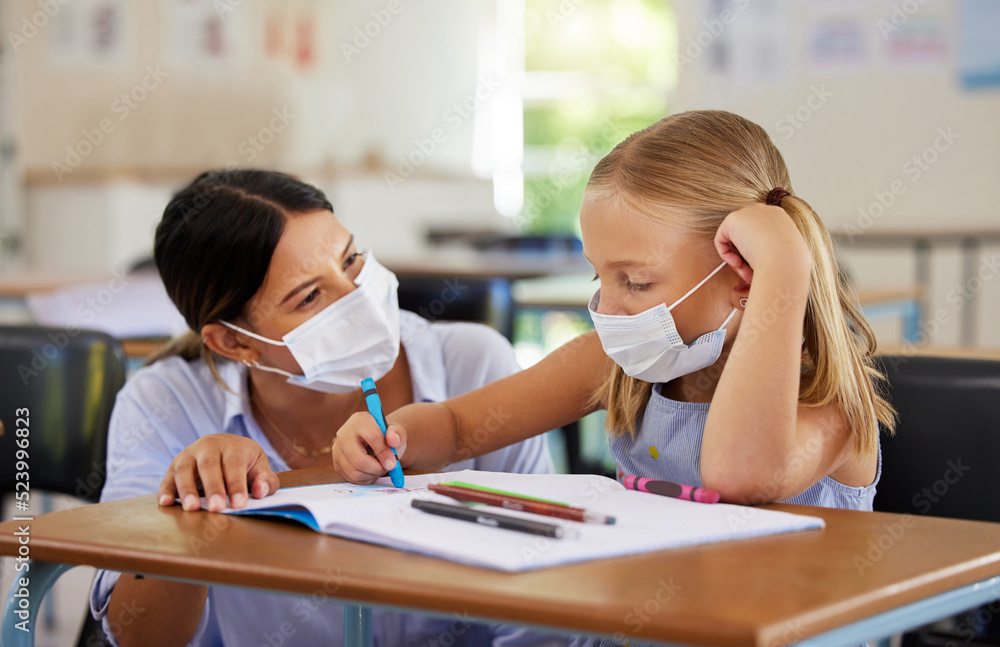 Education, covid and learning with face mask on girl doing school work in classroom, teacher helping student while writing in class. Elementary child wearing protection to stop the spread of a virus Education, covid and learning with face mask on girl doing school work in classroom, teacher helping student while writing in class. Elementary child wearing protection to stop the spread of a virus