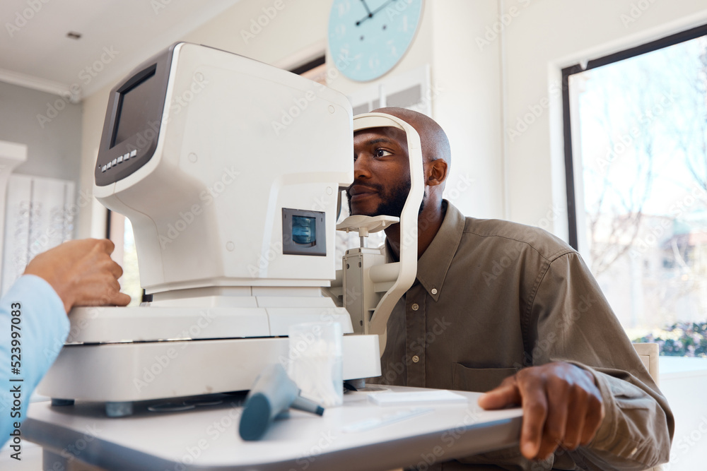 Young African man getting an eye exam by an optometrist with technical optic equipment. Male getting an eyesight test with a autorefractor to get eyewear. Guy at an optical shop for new spectacles.